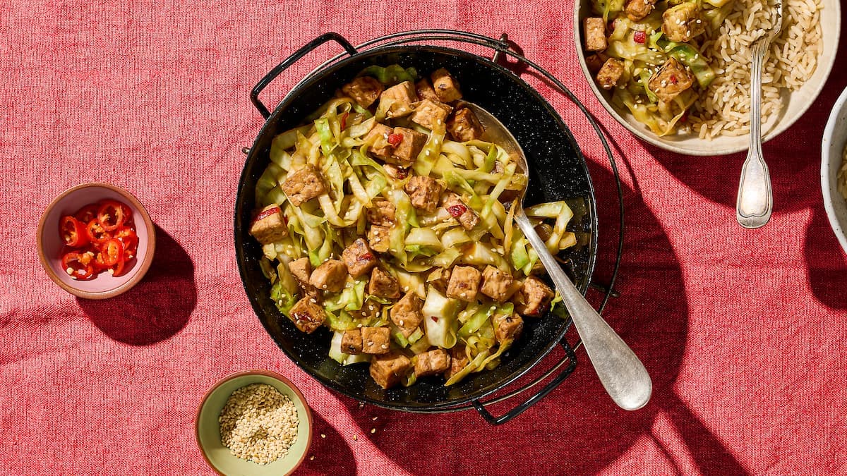 Gemarineerde tempeh met spitskool geserveerd op een bord met knapperige kool en goudbruin gebakken tempé.