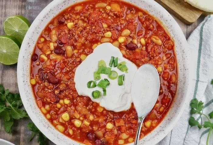 Chili sin carne in een kom met bonen, tomaat en groenten, geserveerd met rijst en verse kruiden.