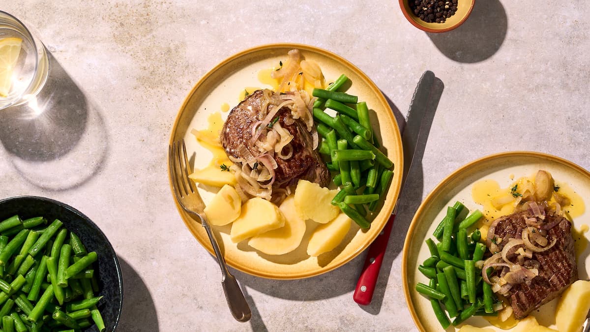 Biefstuk met sjalotten, sperziebonen en aardappelen geserveerd op een bord, met gebakken biefstuk, groene bon