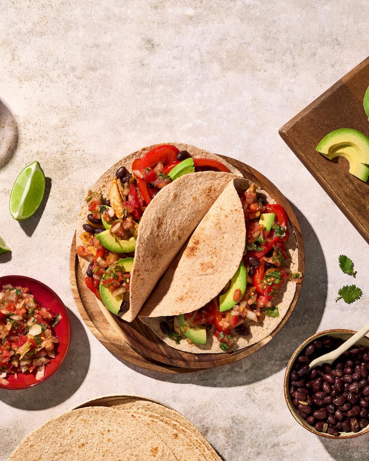 Mexicaanse fajita's met kip, zwarte bonen en avocado, geserveerd met tomaat-uien-salsa en limoen.