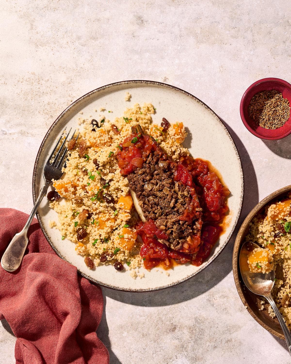 Halve gevulde aubergines in een rijke rode tomatensaus, geserveerd met een luchtige couscous-salade waarin stukjes oranje pompoen zijn verwerkt.