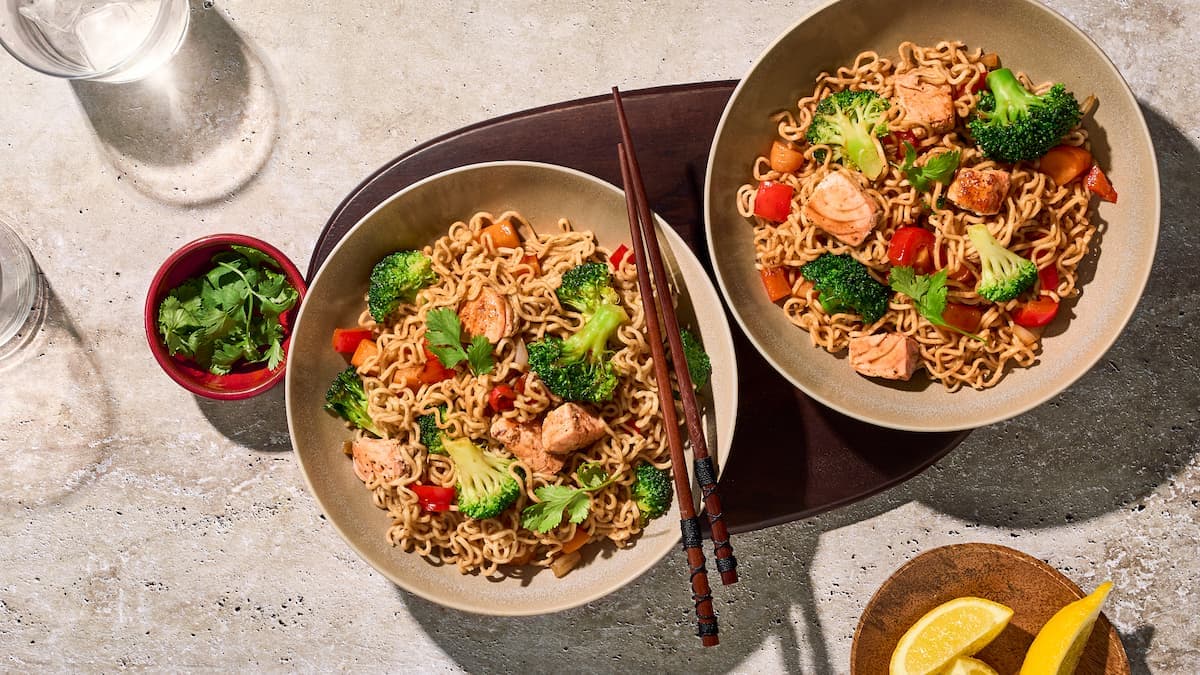 Mie met geroerbakte zalm en groente in een kom, met stukjes zalm, kleurrijke groenten en glanzende mie