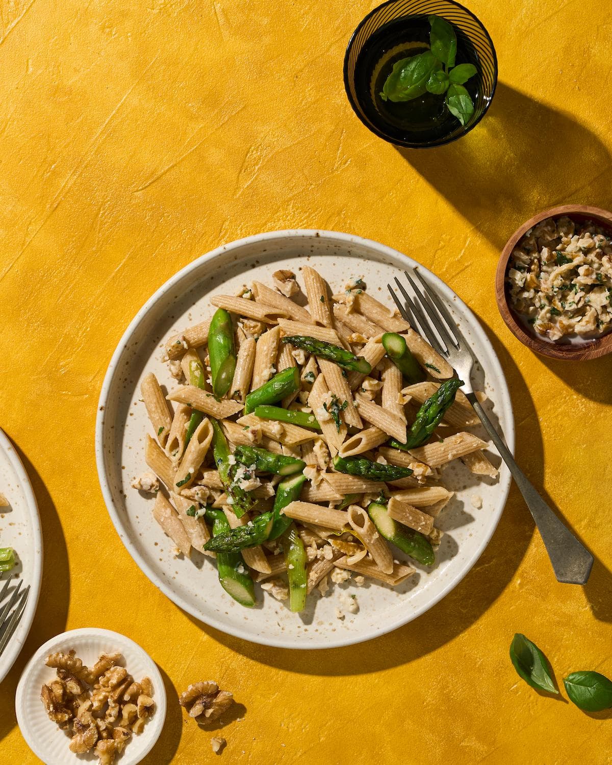Penne pasta gemengd met beetgare stukjes groene asperge en een romige walnotensaus, gegarneerd met gehakte walnoten en verse kruiden.
