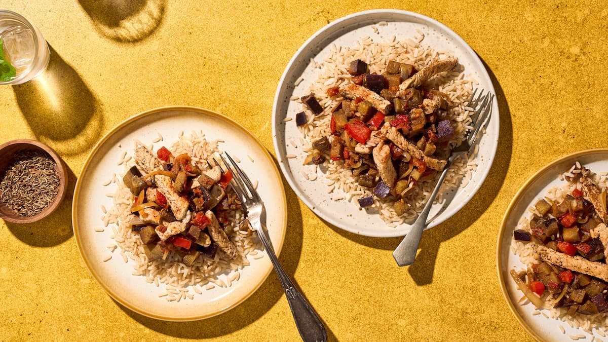 Rijst met een stoof van tomaat, varkensvlees en aubergine geserveerd in een diepe schaal met saus en verse kruiden.