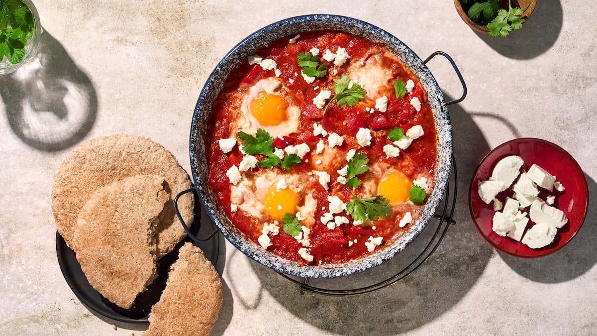 SShakshuka met paprika in een pan, geserveerd met tomatensaus, gepocheerde eieren en verse kruiden