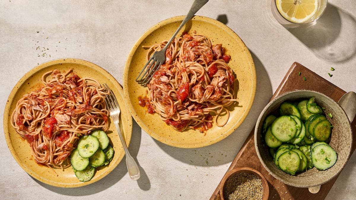 Spaghetti met tomaten‑tonijnsaus en komkommersalade, geserveerd als pastagerecht met tomatensaus, tonijn en frisse salade op een bord