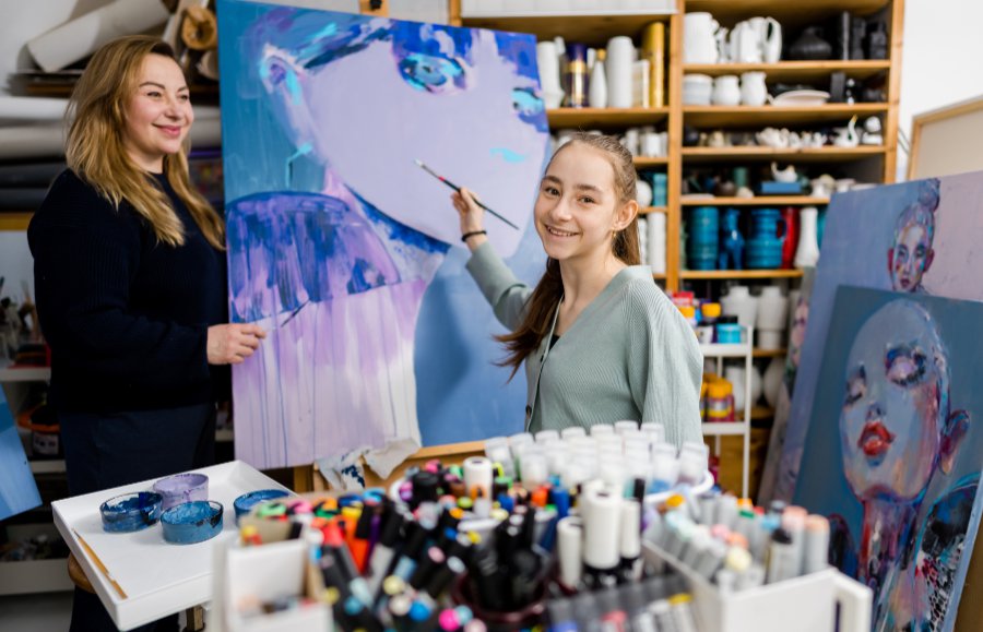 Meisje houd penseel vast een staat voor een schilderij met blauwe kleuren